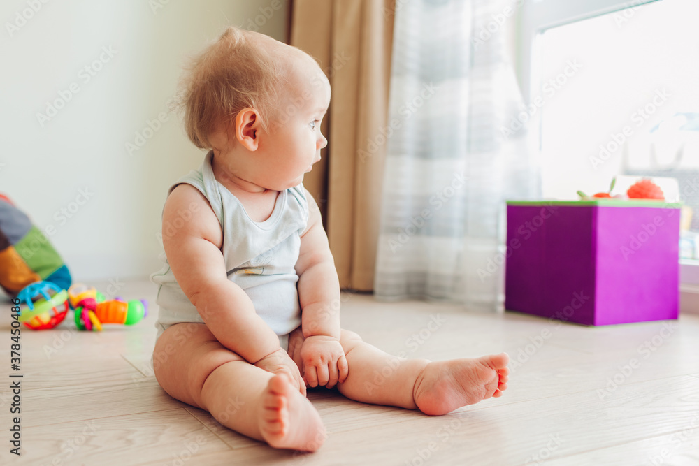 Little newborn baby playing with toys sitting on floor at home. Kid looking at window Little newborn baby playing with toys sitting on floor at home. Kid looking at window