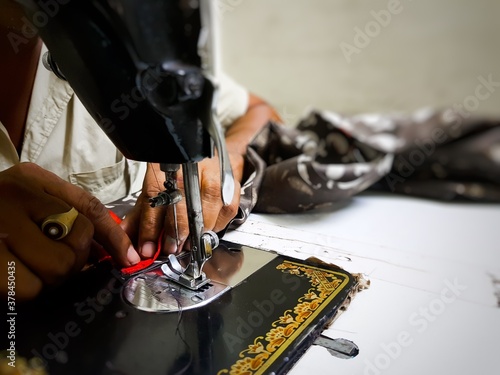 Close up photo of manual sewing machine with tailor hands stitching red cloth with selective focus photo