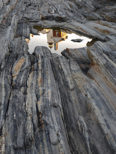 Maine's Pemaquid Lighthosue reflected in a tidal pool on the coastal rocks that line the shore at sunrise photo