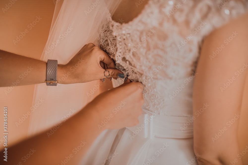 The back of the bride in a wedding dress. Mom's and woman's hands help fasten the clasps at the back. The back of the bride in a wedding dress. Mom's and woman's hands help fasten the clasps at the back.