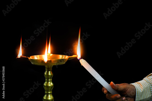 oil brass lamp diya being lit by a candle for inauguration ceremony holy worship in isolated dark black background
