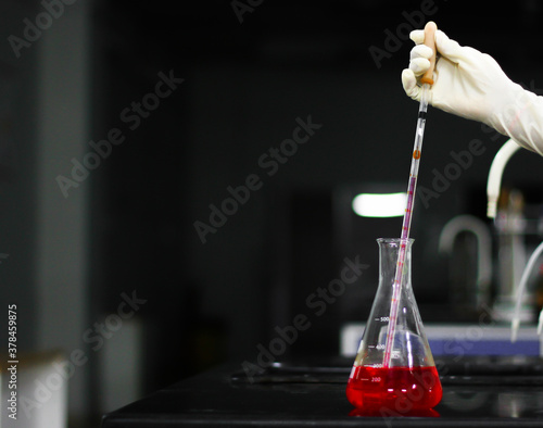 aspirating a red chemical on a glass conical flask with a pipette in a chemistry lab photo