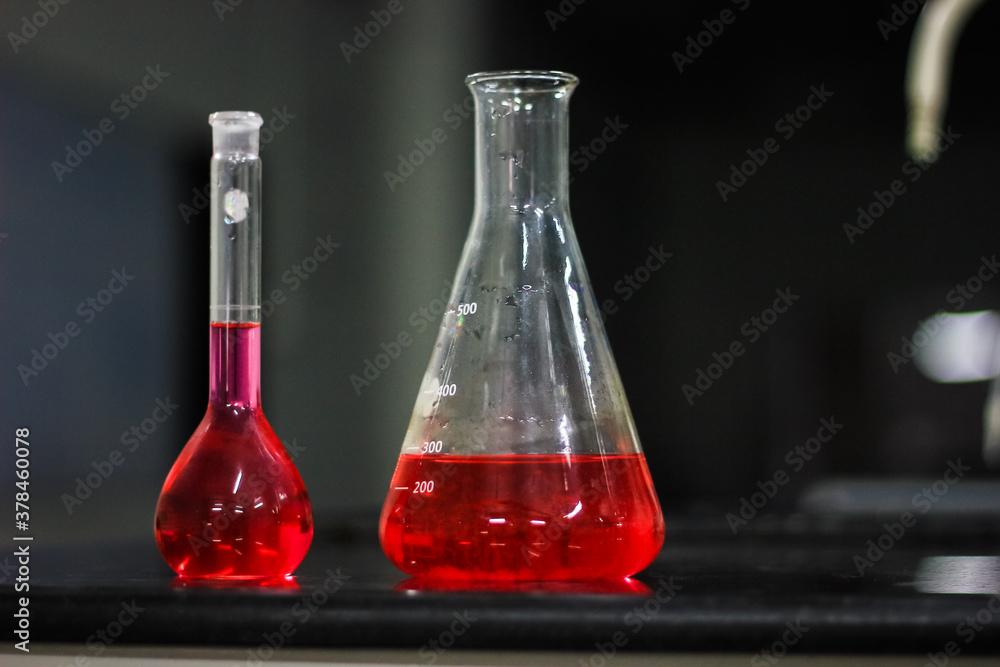 red liquid in a conical flask and round bottomed flask on a black granite table in dark background red liquid in a conical flask and round bottomed flask on a black granite table in dark background