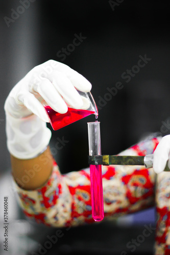 pouring a red liquid from a glass beaker to a test tube with a gloved hand in a chemistry lab photo