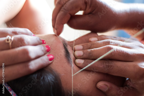 shaping and plucking of eye brow with threading. epilation cosmetic procedure in beauty parlour.