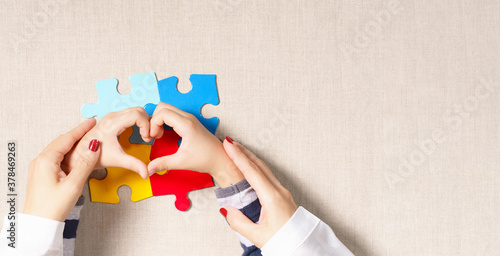 Foto Top view, hands of mother holding hands of little autistic child making heart shape over colorful puzzle pieces