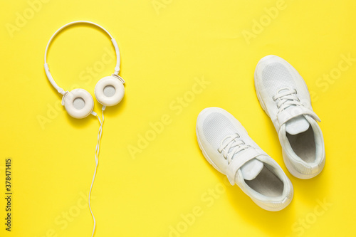 Headphones and sneakers are white on a bright yellow background.