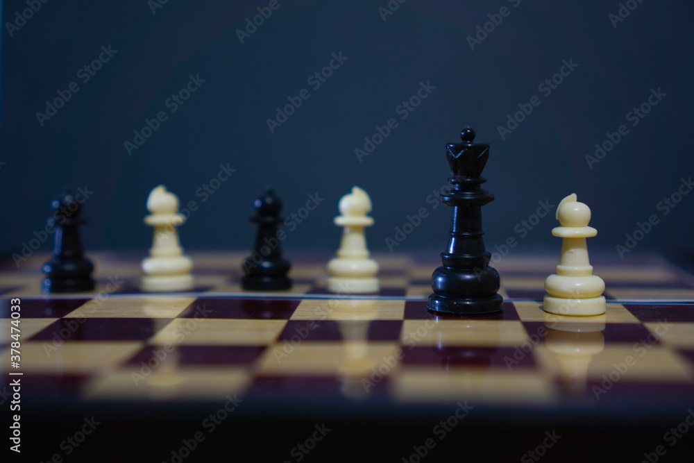 Black queen chess piece with pawns softly blurred in background