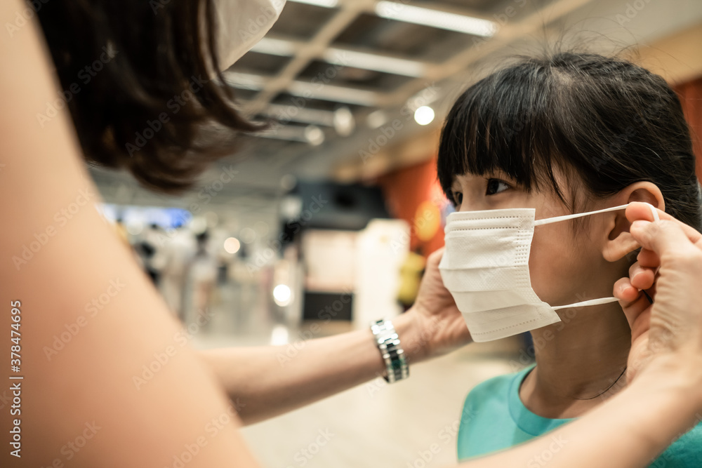 Asian young mother wearing mask for little kid in department store