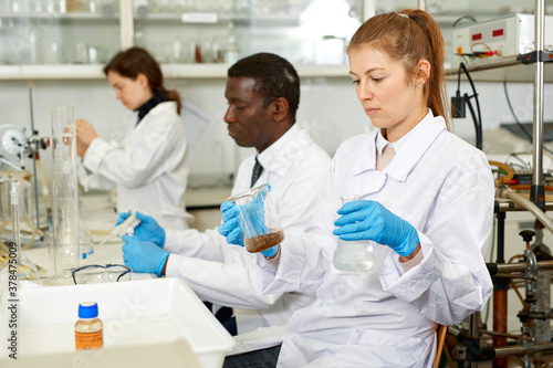 Focused women lab technicians in glasses working with reagents and test tubes  man on background