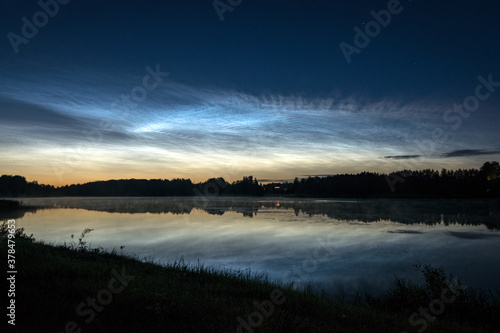 night landscape with white silver clouds over the lake  blurred foreground  charming cloud reflections in the lake water  summer night