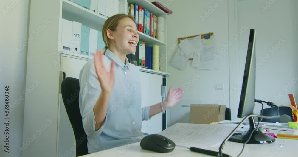 An Young Blond Woman with Earphones is Making a Video Conference Call with a Computer to Colleagues While Smart Working Alone in the Office. An Young Blond Woman with Earphones is Making a Video Conference Call with a Computer to Colleagues While Smart Working Alone in the Office.