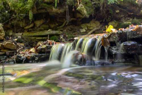 a small rapid river flows through dolomite rocks, long-term exposure, gentle and fuzzy river water, colorful autumn leaves and dry branches water
