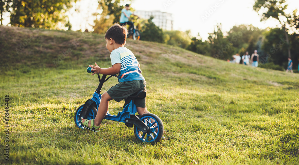 Caucasian boy with a bike is riding on the grass during a walk in park with his parents Caucasian boy with a bike is riding on the grass during a walk in park with his parents