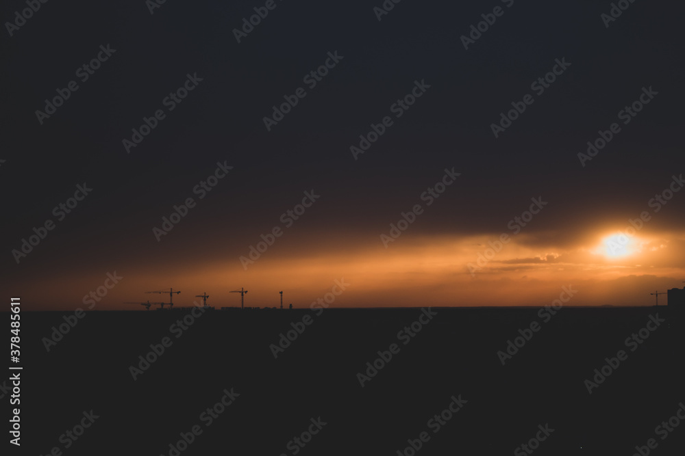 Tower cranes and buildings on horizon with evening sky, soft focus. Sunset over city. Construction with scenic evening sky and clouds above. Picturesque cityscape in evening haze. 