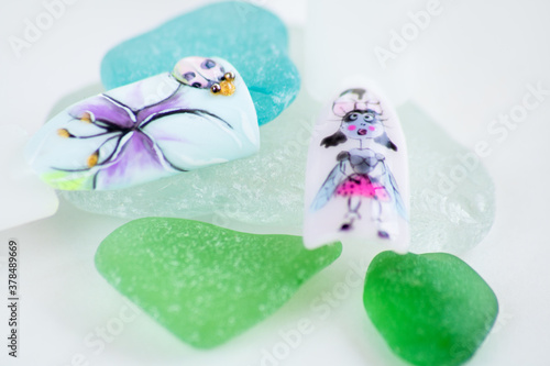 Fototapeta Naklejka Na Ścianę i Meble -  nail samples with a fly in a dress and ladybug, manicure design. on pieces of the colored glass at the white background
