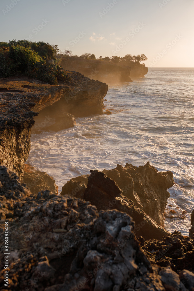 Vertical shot sunset seascape with rocky beach and crashing waves