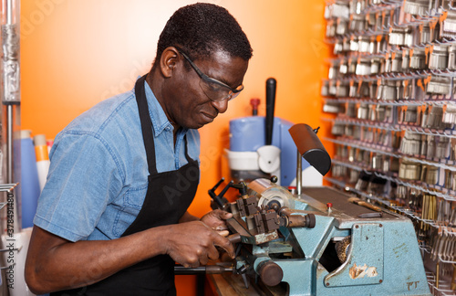 Serious African-American man working in key workshop, making key copies on bench machine