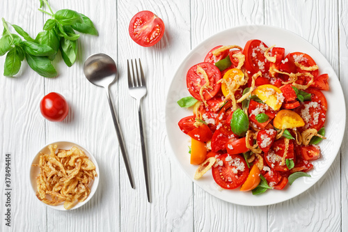 tomato salad with crispy fried onion, quinoa and fresh basil on a white plate on a wooden table, close-up, landscape view from above, flat lay