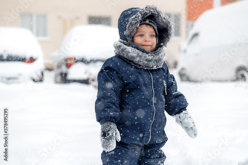 Adorable baby boy in a warm white snow suit walking on snow.
