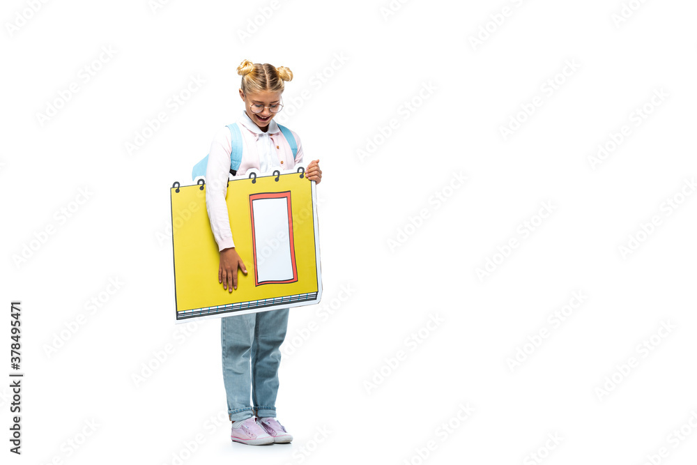 full length view of joyful schoolgirl in eyeglasses holding paper cut notebook on white full length view of joyful schoolgirl in eyeglasses holding paper cut notebook on white