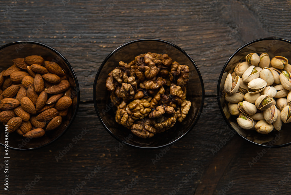 Fototapeta premium Almond, pistachio and walnut in a small plates which standing on a black table. Nuts is a healthy vegetarian protein and nutritious food.