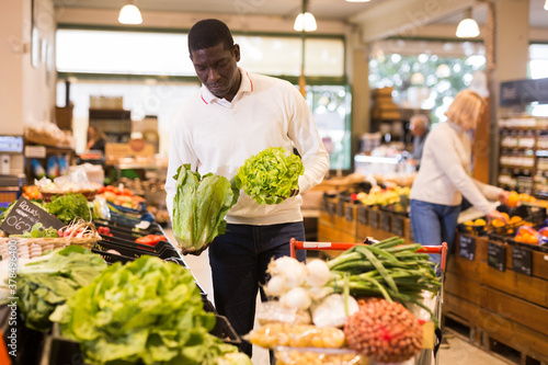 African American man shopping in organic food store, choosing fresh vegetables
