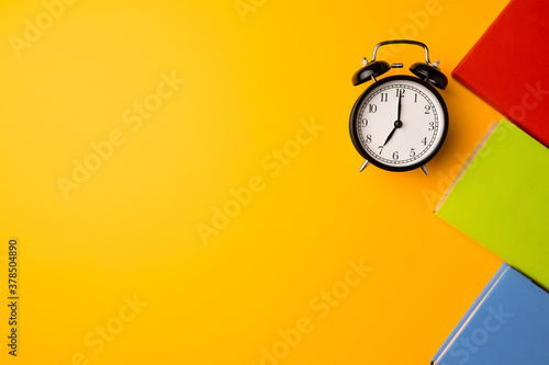 Three color hardcover notepads and alarm clock on yellow background