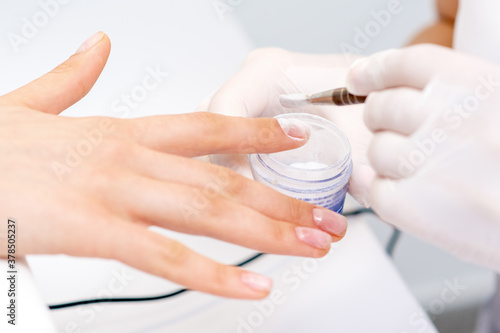 Close up of the process of applying acrylic powder on the nails of a young woman in a beauty salon