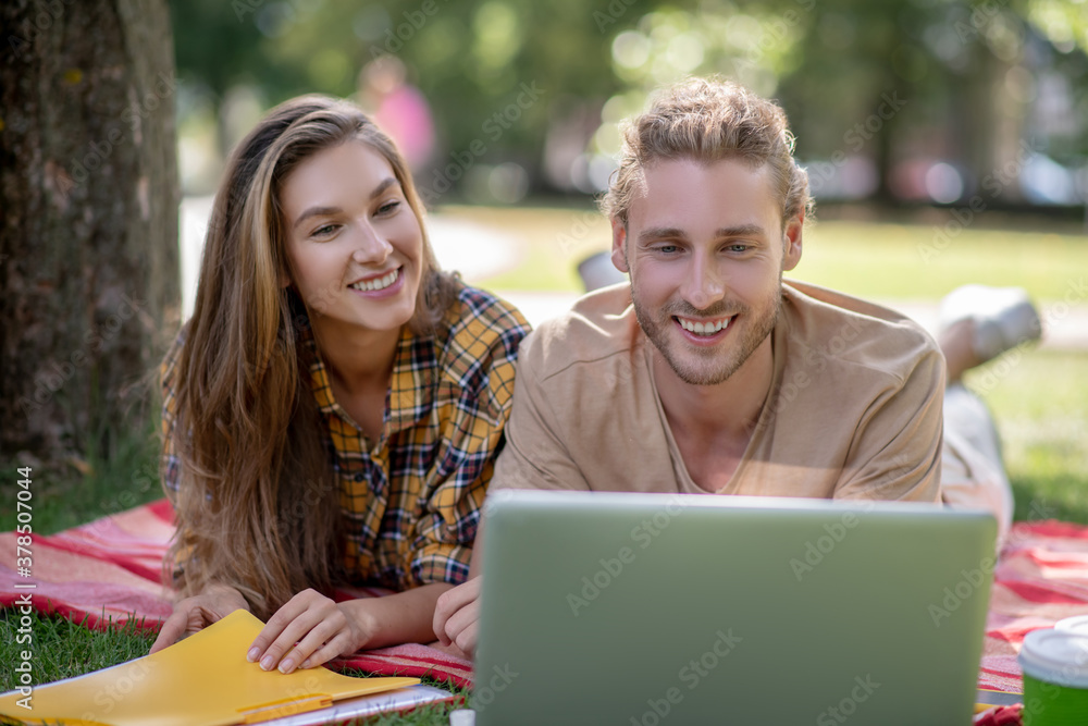 Young couple lying on the grass and watching something on a laptop Young couple lying on the grass and watching something on a laptop
