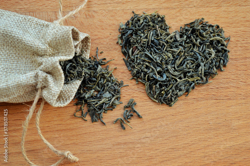 Heart made of loose leaf tea and jute bag on wooden background.