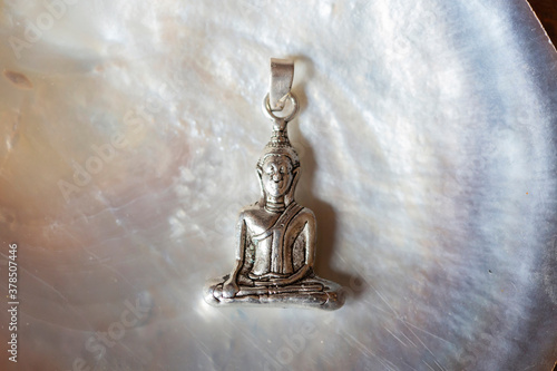 Beautiful silver Buddha pendant jewelry on pearly white shell background