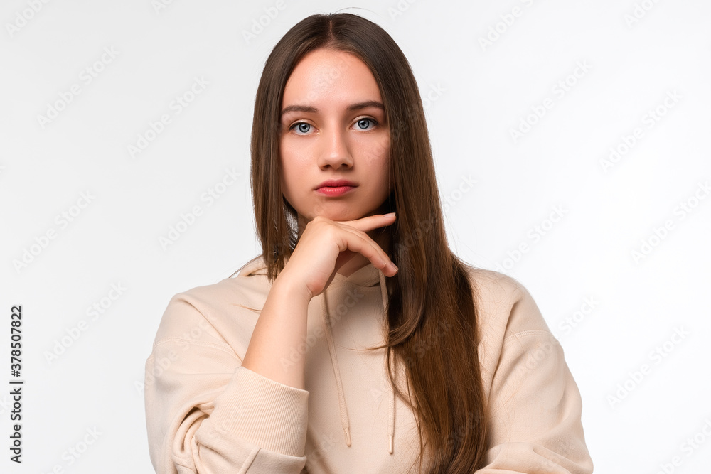 Photo of Thoughtful young woman with long chestnut hair standing with hand raised on chin Photo of Thoughtful young woman with long chestnut hair standing with hand raised on chin