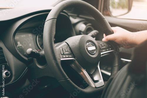 Closeup male hand driving a car with interior luxury dashboard and steering wheel.