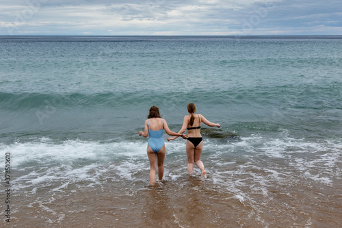 Two girls in swimming suits going into water of Baikal lake on stormy weather in summer