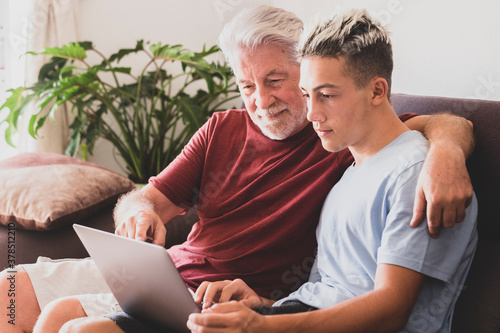 A white haired grandfather and teenage grandson are looking at the same laptop computer sharing the same passion or interest - friendship and family love concept