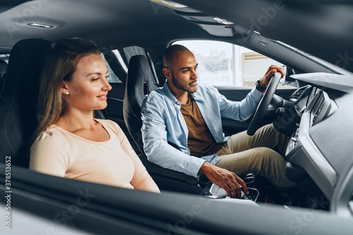 Joyful young couple looking around inside a new car they are going to buy in a car shop