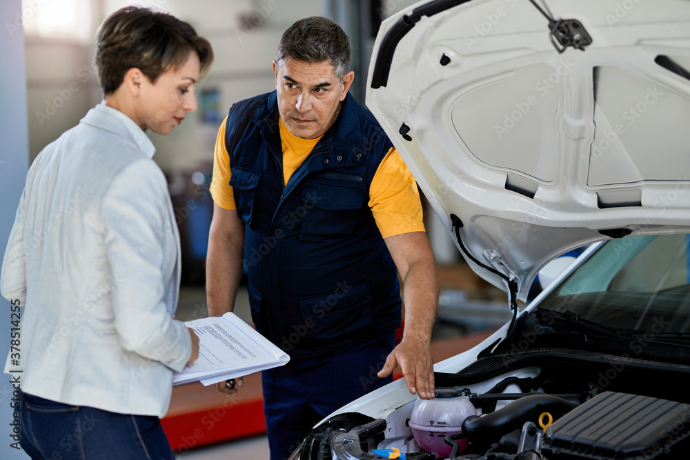 Auto repairman explaining car engine malfunction to a businesswoman in a workshop. Auto repairman explaining car engine malfunction to a businesswoman in a workshop.