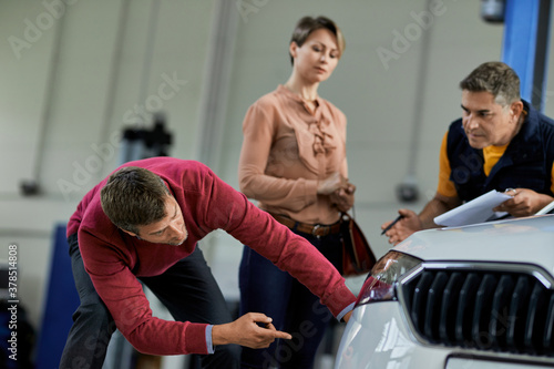 Male customer examining his car while being at auto repair shop.