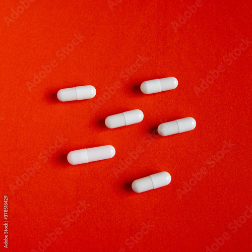 White tablets capsules on a red background, search for medicines, fight against diseases and for health, search for a remedy for coronovirus