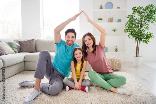 Full size photo of positive three people mommy daddy small kid girl make hands roof enjoy loan house sit comfort carpet floor in living room indoors photo