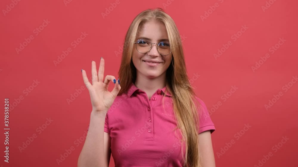 Happy young woman showing ok sign with fingers and winking isolated on a red background. Happy young woman showing ok sign with fingers and winking isolated on a red background.
