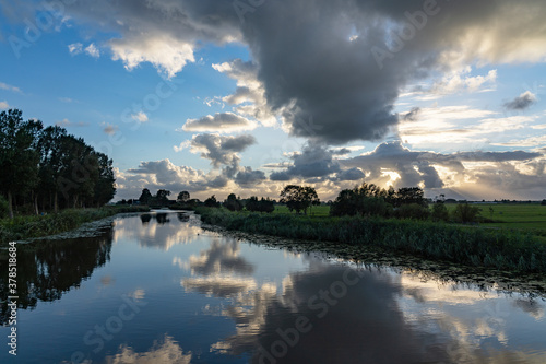 Beautiful sunbeams through the dark clouds during sunset above the canal of the Geerpolder near Zoetermeer © Emma