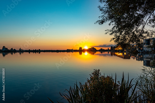 The rising sun has completely dissolved the morning mist above lake Noordhovense plas and the smooth water reflects the horizon beautifully