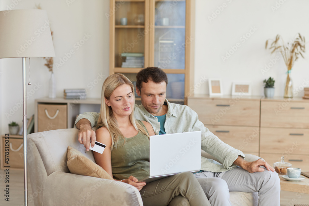 Young couple sitting on sofa with laptop they shopping online and using their credit card in the living room