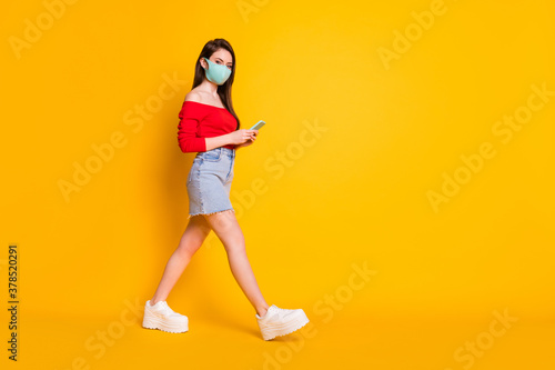 Full size profile side photo charming girl medical mask go walk travel copyspace use smartphone wear red top denim jeans short mini skirt legs isolated bright shine color background © deagreez