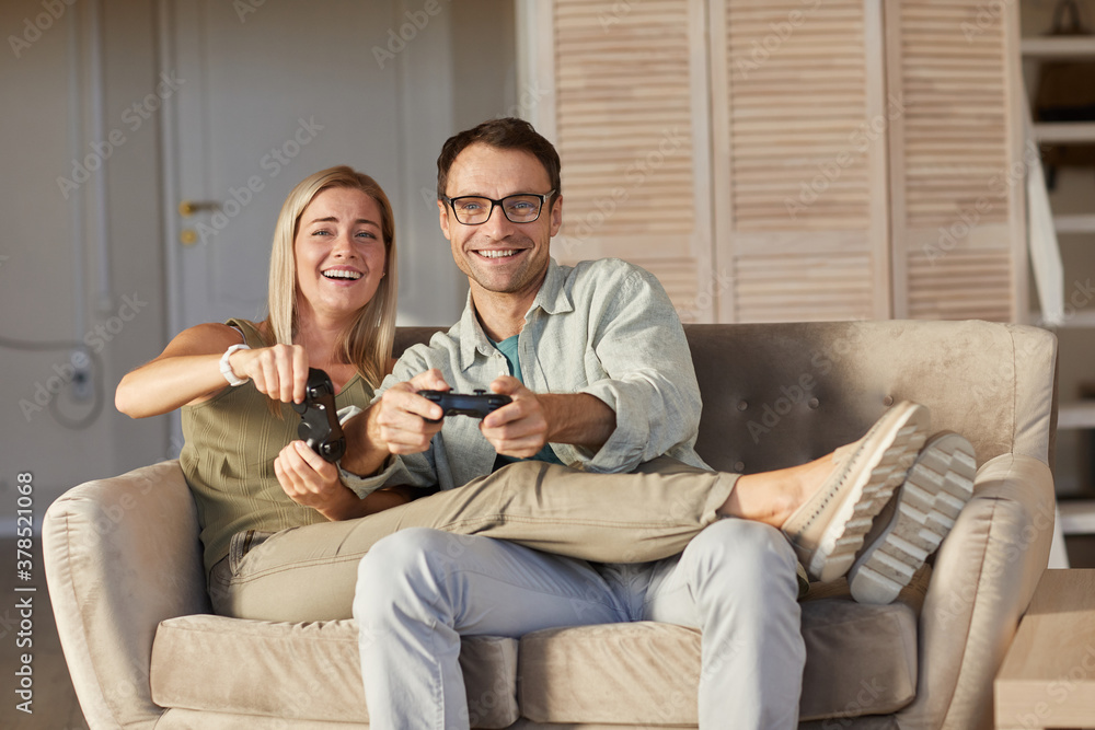 Portrait of young couple smiling at camera while having fun during play in computer games at home Portrait of young couple smiling at camera while having fun during play in computer games at home