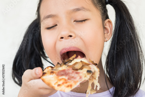 cute little girl holds piece of pizza  hungry student opens mouth wide while sees delicious slice of pizza  wants to eat  positive woman with junk food  people and eating  people and snack concept.