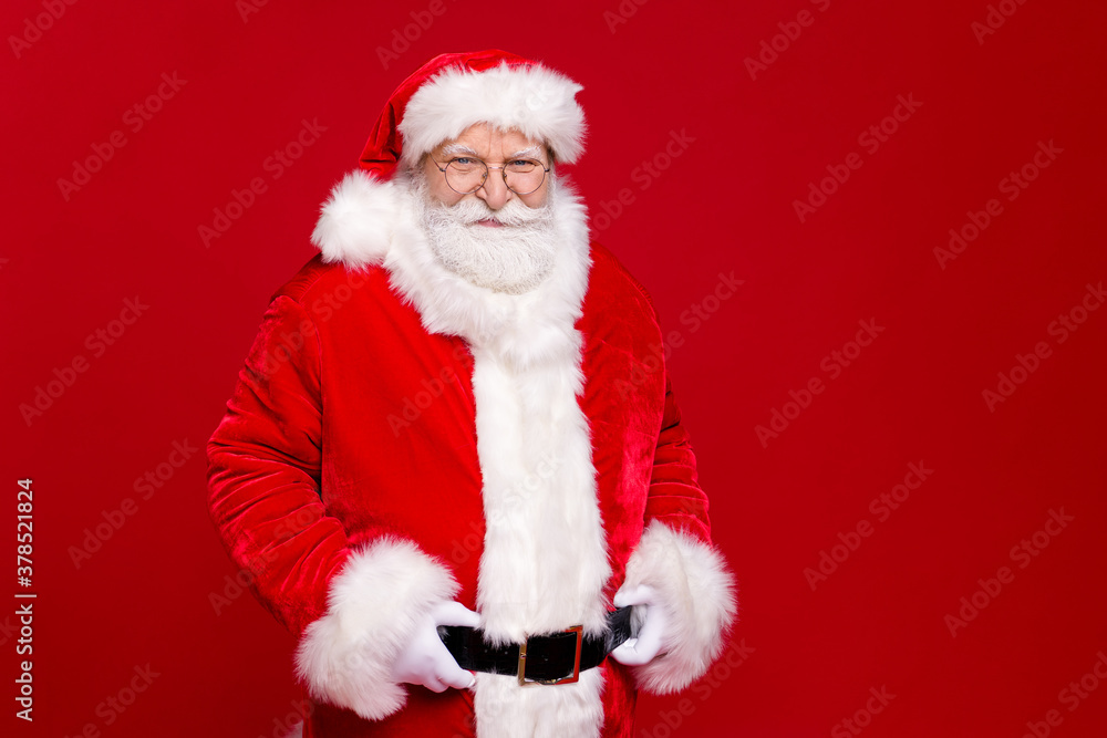 Photo of pensioner old man grey beard hand hips self-assured certain look wait midnight wear santa costume leather belt gloves coat spectacles headwear isolated red color background