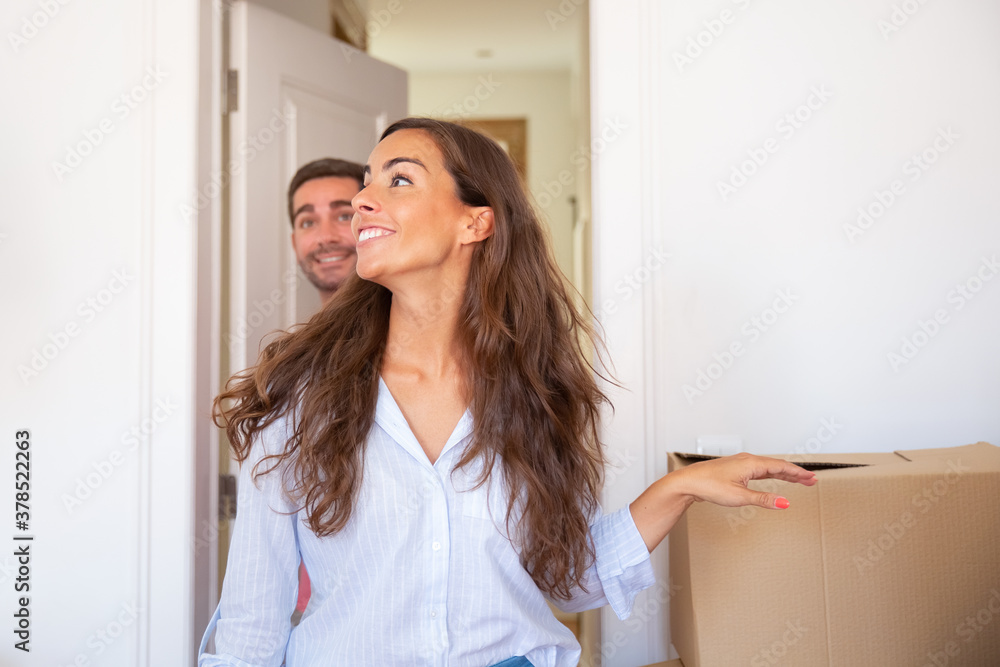 Joyful young man and woman walking through doorway and looking around in their new apartment with carton boxes. Medium shot. New home or surprise concept Joyful young man and woman walking through doorway and looking around in their new apartment with carton boxes. Medium shot. New home or surprise concept